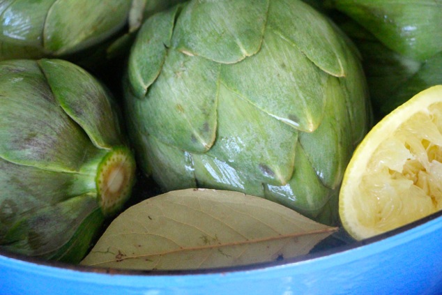 adding bay leaf to artichoke pot