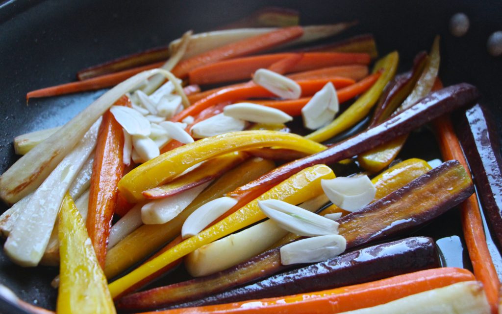 adding garlic to carrots in pan